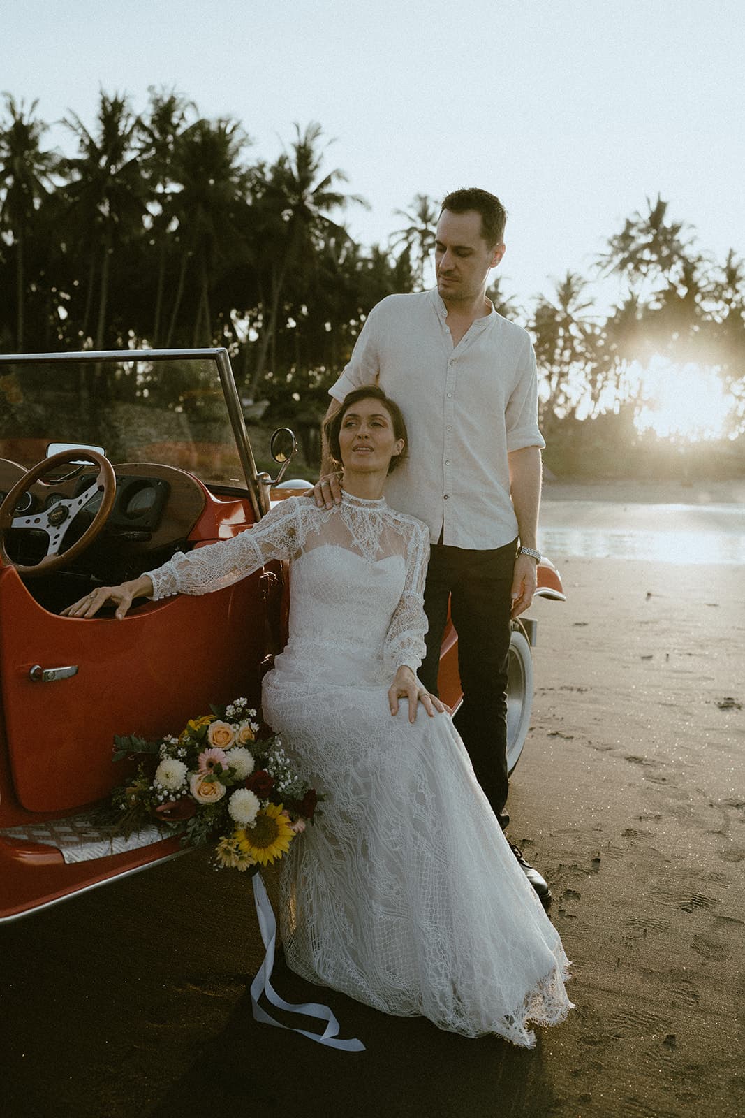 A couple sharing a sunset moment beside a vintage red car
