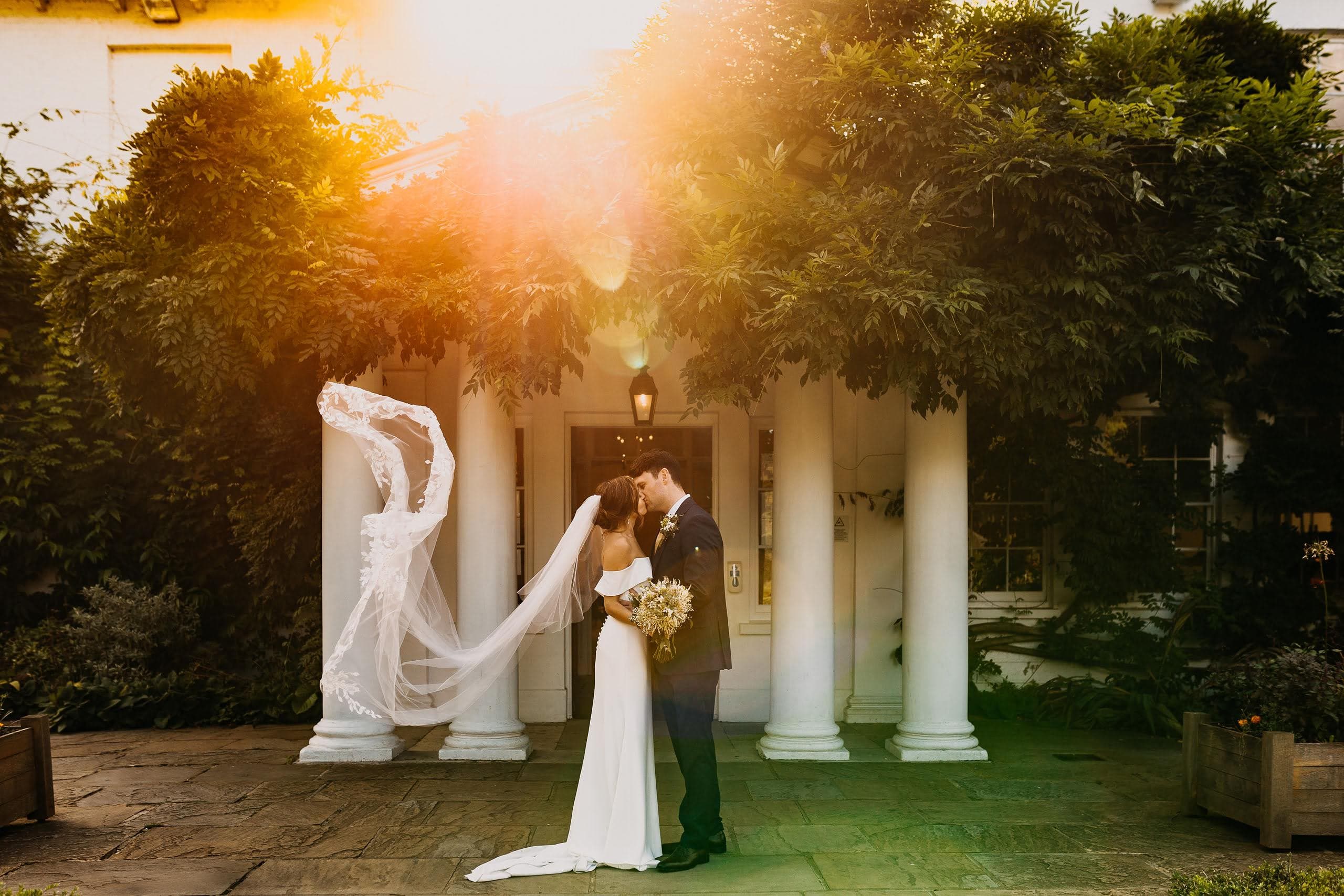 A newlywed couple kissing outside their UK wedding venue in golden sunlight