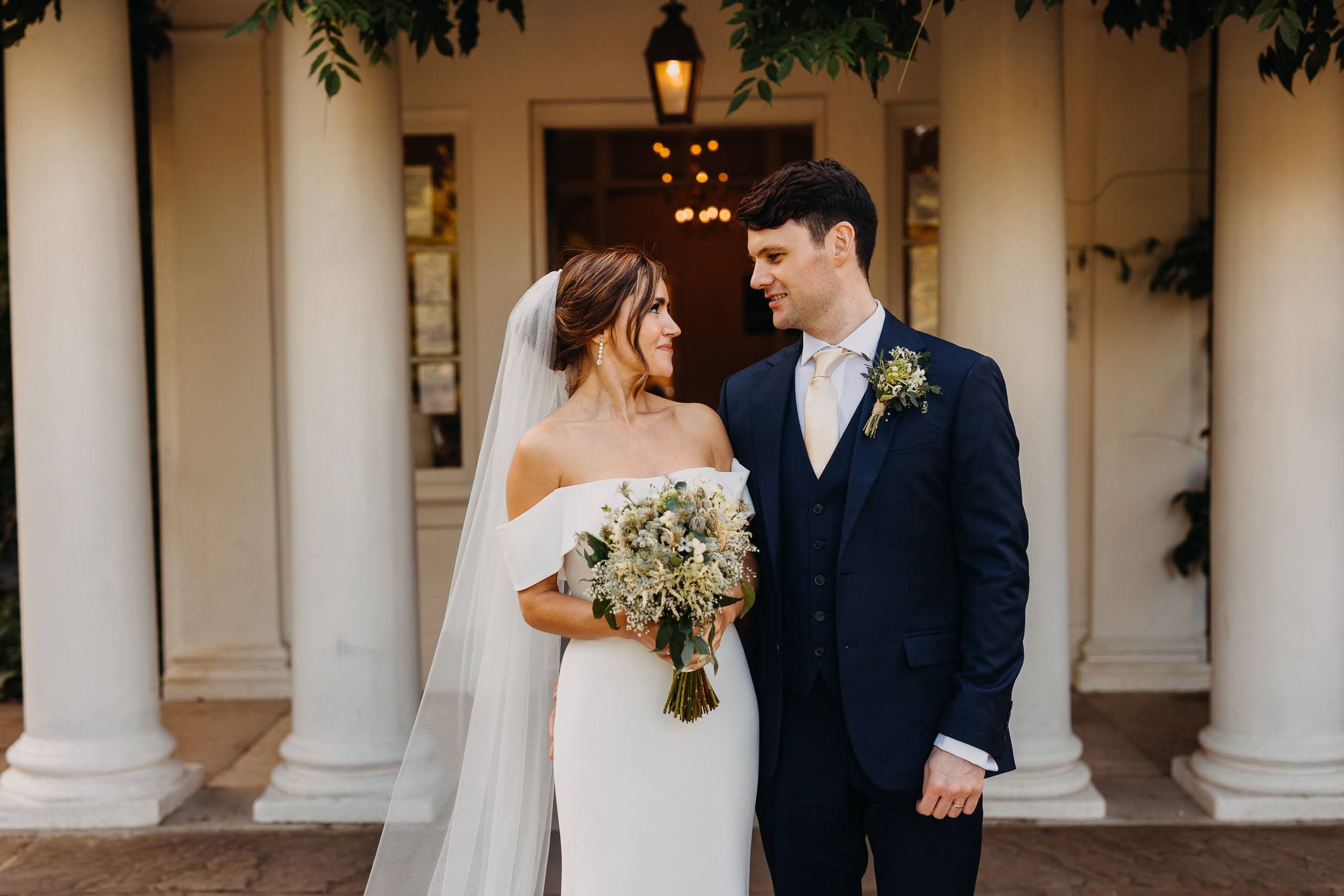A bride and groom standing together outside a columned UK wedding venue