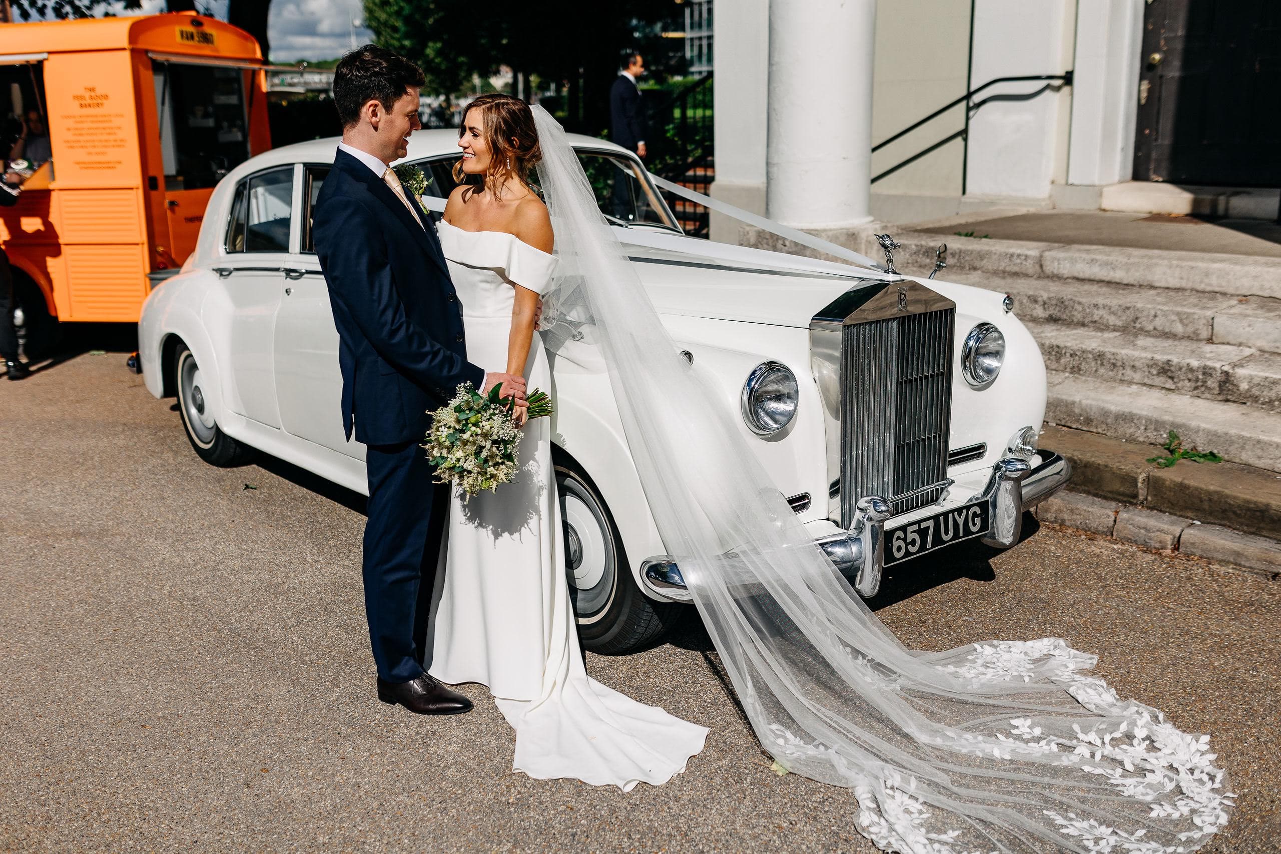 A newlywed couple standing beside a white vintage wedding car